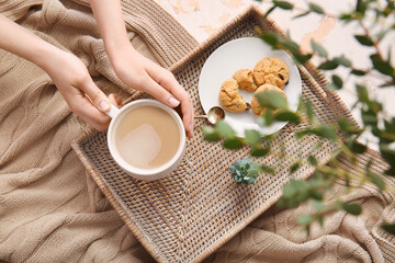 Female hands with cup of coffee and cookies on tray