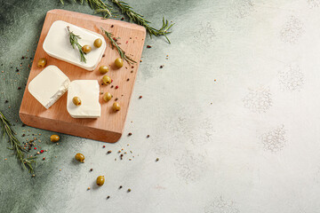 Tasty feta cheese with olives and spices on color background