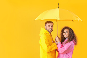 Happy young couple with umbrella on color background