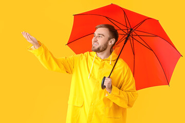 Handsome young man with umbrella on color background