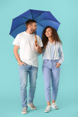 Happy young couple with umbrella on color background
