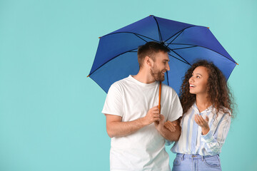 Happy young couple with umbrella on color background