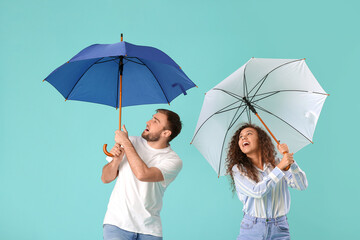 Happy young couple with umbrellas on color background