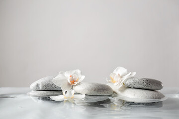 Spa stones and flowers in water against light background