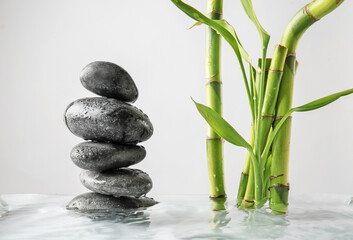 Stack of spa stones and bamboo in water against light background