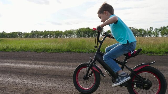 A boy rides a bike on a country road on a Sunny day. A happy child rides a Bicycle, gaining speed. Active rest in the open air, the achievement of the goal.
