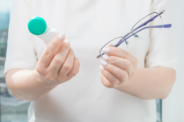 women choosing between eyeglasses and contact lenses. holds glasses in one hand and one-day contact lenses in the other. problems with vision, eyesight concept