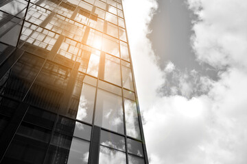 Facade texture of a glass mirrored office building. Fragment of the facade. Bottom view of modern skyscrapers in business district in evening light at sunset with lens flare filter effect. Black and w