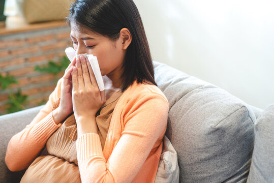 Asian pregnant woman sneezing she use tissue to cover her nose.
