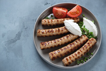 Round grey plate with grilled serbian cevapi or cevapcici sausages and kajmak cheese, studio shot...