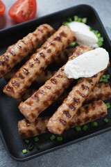 Close-up of roasted cevapci or skinless beef sausages topped with kaymak cheese, vertical shot, selective focus