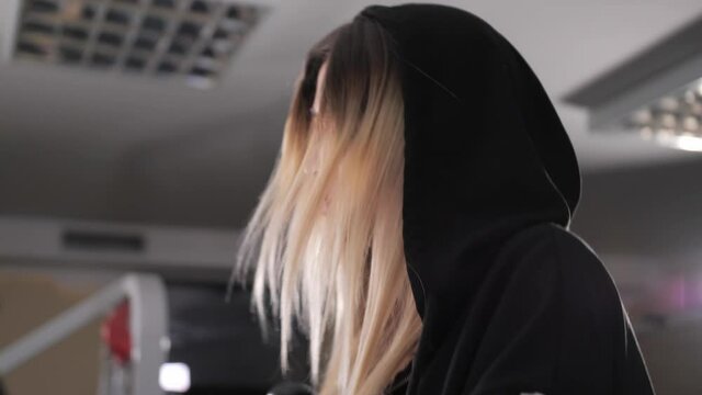 Pretty girl in a black jacket with a hood runs on the orbitrek in the gym.Hard cardio workout.Attractive young girl running in gym.