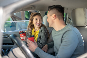 Woman and man sitting in car with glasses of coffee.