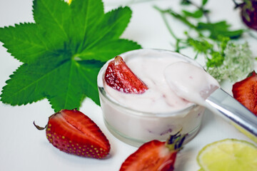 DIY homemade strawberry facial mask. A glass bowl with a pink mass of cream and strawberries next to a sprig of green plants, halves of fresh berries, lime, a brush for  masks on a white background