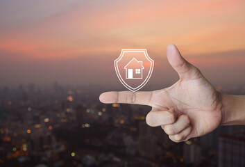 Hand pressing house with shield flat icon over blur of cityscape on warm light sundown, Business home insurance and security concept