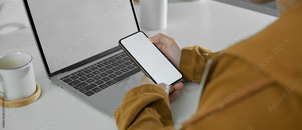 Wall mural Female freelancer working with mock-up smartphone and laptop on simple workspace