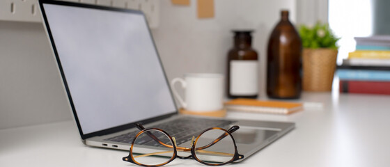 Home office desk with mock-up laptop, glasses, cup and decorations on white table