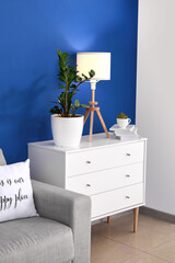 Chest of drawers with glowing lamp and houseplant in room