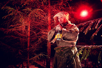 Obraz premium Medieval monk in canvas sackcloth robe with lattern in dark forest with snow and red light on winter night. Fantasy or fairy tale about wandering monk. Story about the forces of good and evil in world