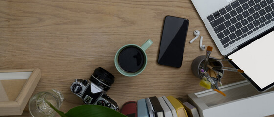 Overhead shot of wooden table with digital devices, camera, painting brush , coffee mug and copy space