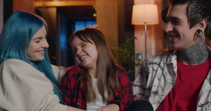 Portrait of happy family having fun and laughing while sitting on couch. Modern parents with piercing and tattoos and their kid spending time together at home. Concept of leisure.