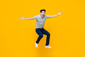 Young cheerful energetic handsome Asian man jumping with open hand gesture isolated on yellow studio background