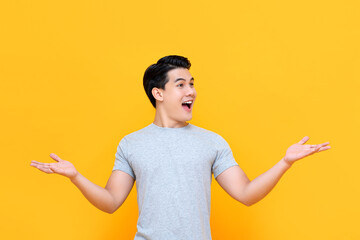 Half body portrait of smiling excited Asian man in gray t-shirt with open hand gesture in yellow...