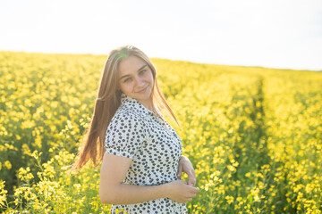 Naklejka na ściany i meble Beautiful girl in a rapeseed field, with her hair in the sun.