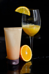 tube of cosmetic with fresh oranges on a black background