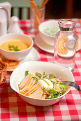Chicken Caesar salad served in a white bowl. Traditional salad with chicken meat, eggs, tomatoes. Dinner in restaurant.