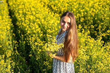 Naklejka na ściany i meble Girl in a rapeseed field in the sun.