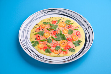 Chilled cucumber avocado soup with salmon fish, tomato, pepper, fresh greenery served in a plate over blue background.
