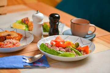 Salad with meat and vegetables. Italian cuisine, different dishes served in restaurant on light rustic wooden table.