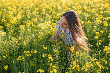 Naklejka na ściany i meble A girl in a canola field, with her hair loose, sniffs canola.