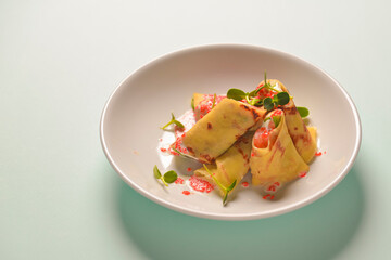 Crepes stuffed with cream cheese and salmon with sour cream sauce and red caviar over pastel blue mint background.