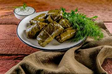 Homemade dolma on a wooden background with herbs, spices and sour cream sauce.