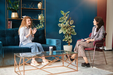 Happy red-haired woman talking to a female psychologist. Discusses her problems, mental trauma. Consultation in the office on the sofa. Positive mood.