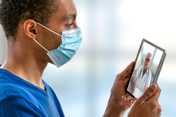 view of a afro-american young man with aCovid 19 proctection mask having an online consultation with his doctor