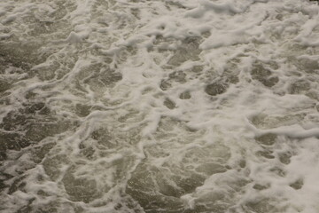 filled frame full screen desktop wallpaper background shot of greenish troubled wavy sea water with white foam