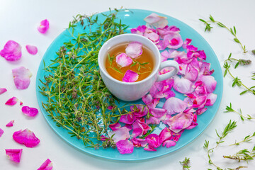 Homemade herbal tea in a white cup. Tea rose petals and thyme on a plate - ingredients for hot healthy drink 