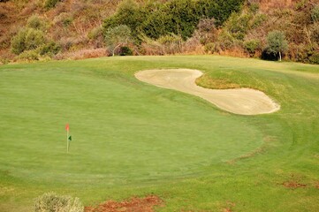 Fototapeta premium Elevated view across a golfing green, bunker and flag near Marbella, Spain.