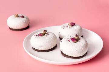 Mousse pastry dessert covered with white chocolate and decorated with rose buds on pastel pink background. Modern stylish cake. Copy space. Close-up.