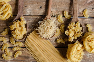different types of raw pasta on a wooden background in
 wooden spoons