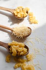 different types of raw pasta on a white background in
 wooden spoons
