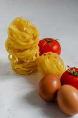 raw tagliatelle pasta with eggs, tomatoes and bell peppers on the table