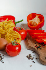 raw tagliatelle pasta with eggs, tomatoes and bell peppers on the table