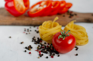raw tagliatelle pasta with eggs, tomatoes and bell peppers on the table
