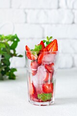 Water with ice, strawberry syrup, fresh strawberries and mint in a glass cup on a white background. A refreshing strawberry drink.
