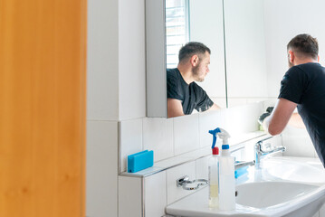 Fototapeta premium professonal cleaner cleaning a bathroom and the glass shelves in the bathroom cabinet