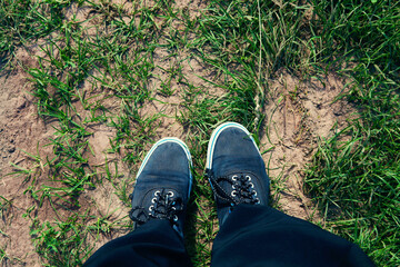 Legs in old worn sneakers on road with grass, top view.